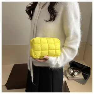 Close-up of a bright yellow quilted puffer cosmetic pouch held against a white sweater
