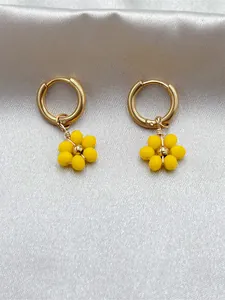 Vue détaillée de breloques fleurs en perles jaunes sur des créoles en acier doré.