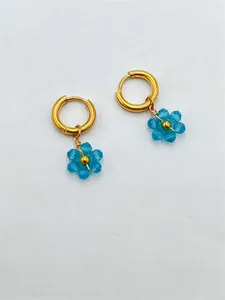Détail de breloques fleurs en perles bleues faites à la main sur créoles dorées.