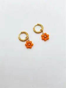 Vue détaillée de boucles d'oreilles créoles avec fleurs en perles orange.
