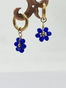 Vue détaillée de créoles dorées en acier avec des pendentifs fleurs en cristal bleu.