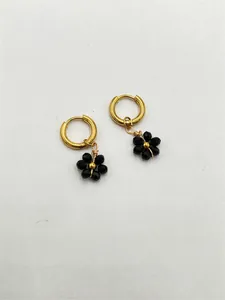 Détail de boucles d'oreilles faites main avec fleurs noires en acier inoxydable doré
