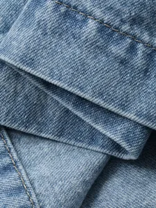 Close-up of light blue denim fabric with detailed stitching and woven texture