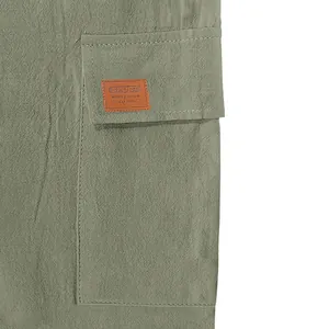 Macro view of green linen cargo shorts pocket featuring a brown leather brand patch