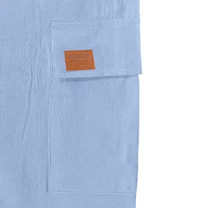 Macro view of side cargo pocket with decorative patch on light blue linen shorts.