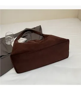 Detailansicht einer braunen Wildleder-Umhängetasche auf einem weißen Bett-Setting