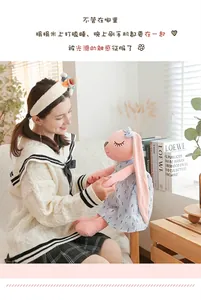 Detailed view of a soft pink rabbit plush toy in a blue floral dress on a sofa.