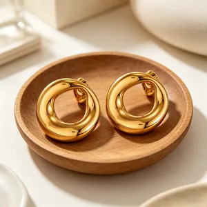 Detail view of chunky golden round earrings on a minimalist wooden tray display.