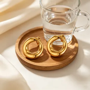 Elegant minimalist chunky gold hollow circle stud earrings displayed on a rustic wooden tray