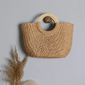 Bohemian straw woven handbag with round wooden handles shown on a neutral gray background
