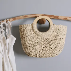 Detail view of handmade woven straw bag with smooth circular wooden handle for beach.