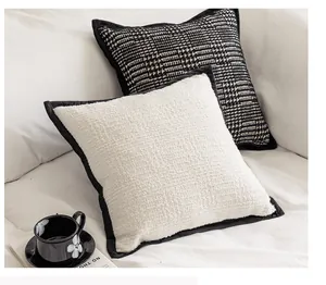 Detailed view of a white bouclé textured pillowcase with black piping on a soft sofa