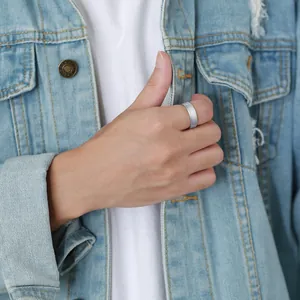 Macro view of a matte silver tungsten steel ring worn on a man's thumb with denim jacket.