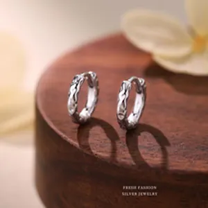 Macro detail of textured S999 silver hoop earrings on a decorative wooden stand.