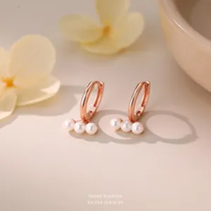 Macro view of elegant rose gold hoop earrings featuring three delicate white pearls