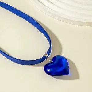Macro view of a blue glass heart pendant on a vibrant blue velvet choker necklace.