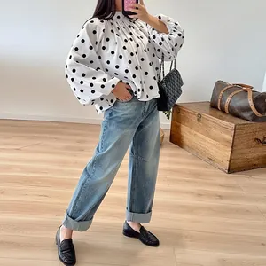 A stylish detail view of a loose white long-sleeve shirt featuring black polka dots