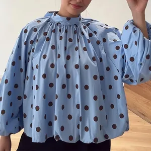 Detailed view of a loose blue mock neck blouse featuring brown polka dots and balloon sleeves.