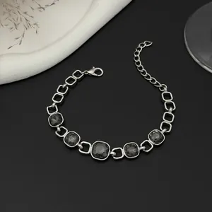 Vue détaillée d'un bracelet à maillons argentés avec des pierres carrées noires facettées.