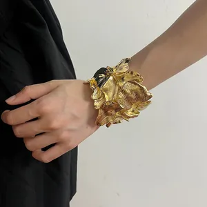 Macro detail view of an oversized vintage gold flower-shaped cuff bracelet on wrist