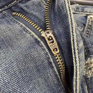Macro view of a high-quality brass YKK metal zipper on vintage blue denim pants
