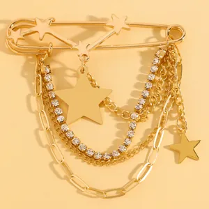 Close-up of gold safety pin brooch with hanging chains, rhinestones, and star charms.