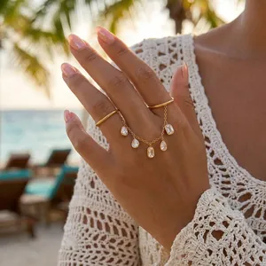 Bague double doigt en acier doré avec pampilles en zircon portée à la plage ensoleillée