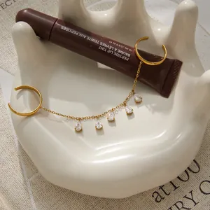 Gros plan d'une bague à pampilles en acier doré avec zircons sur un plat blanc