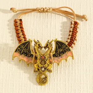 Detailopname van vintage gouden draakarmband met kleurrijke emaille vleugels en gevlochten koord.