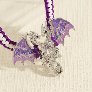Detail van een paarse emaille drakenbedel aan een gevlochten koordarmband in vintage stijl