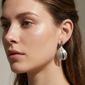 Detailed side view of a model wearing a matte silver floral bud stainless steel earring