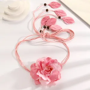 Close-up detail of a bohemian pink fabric rose waist rope with delicate leaf charms