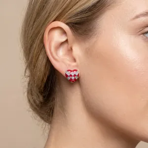Detailed view of a red checkerboard heart earring with small crystals worn on a female ear.