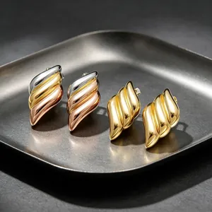 Close-up detail of 18K gold plated wing-shaped earrings in tricolor and gold finishes.