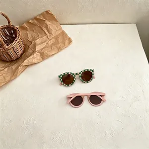Detail of retro checkered and pink sunglasses for kids on a textured white surface