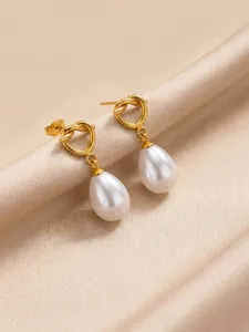 Close-up of gold knotted earrings with teardrop pearl pendants on satin.