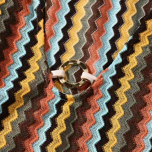 Macro detail showing multi-color zigzag knit fabric and gold ring buckle on dress