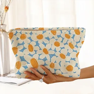 A hand holding a stylish corduroy cosmetic bag with hand-drawn floral pattern and zipper