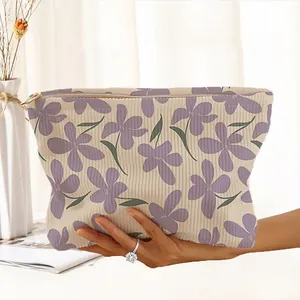 Hand-drawn purple floral corduroy cosmetic bag with gold zipper being held in hand.