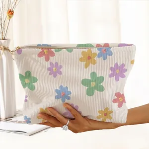 Detailed view of floral corduroy makeup bag held by hand in a bright lifestyle setting.