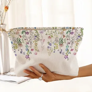 Close-up of white corduroy makeup bag with hand-painted floral print and gold zipper