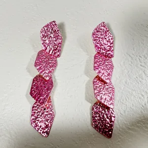 Gros plan de boucles d'oreilles pendantes géométriques roses métallisées martelées