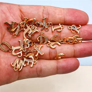 Close-up of gold alphabet charms with rhinestones held in a hand for scale
