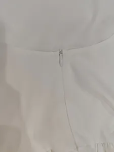 Close-up detail showing the hidden invisible zipper on white sleeveless bubble dress.