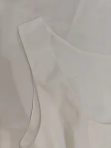 Detailed close-up of white sleeveless dress showing shoulder strap and neckline finish