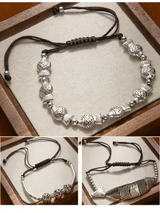 Detailed view of three ethnic style handmade woven bracelets with silver fish charms