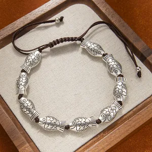 Hand-woven ethnic bracelet with vintage silver fish charms and adjustable brown rope cord.