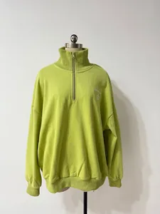 Detalle de sudadera verde lima con media cremallera y bordado blanco en el pecho