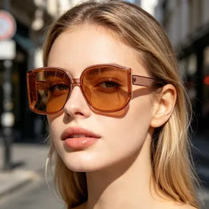 Close-up detail of oversized women's sunglasses with amber lenses on model in sun.