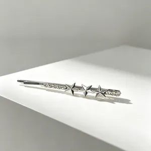 Close-up of silver bobby pin with three stars and sparkling rhinestones on white surface